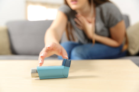 o femeie suferind de astma intinde mana catre un inhalator
